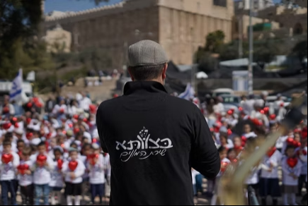 מנחה בצוותא בחולצה ממותגת מול קהל גדול בשירת המונים בירושלים