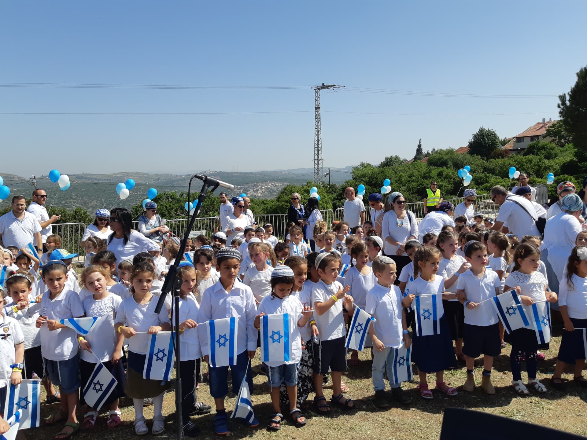 ילדים ומבוגרים בשירת המונים בחוץ עם דגלי ישראל ובלונים